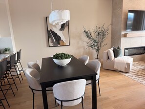Een moderne eetruimte met een donker houten tafel, witte stoelen, een kom met groen en een hanglamp.