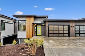 Een modern huis met twee verdiepingen, een garage, een houten accentmuur en een verzorgde voortuin.