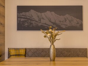 A dining table with a vase of flowers, a plaid pillow, and a wall-mounted painting of mountains. - Arcade Appartement/Fewo 4-Bettwohnung Nr. 115C02 by Interhome (Saas-Fee)
