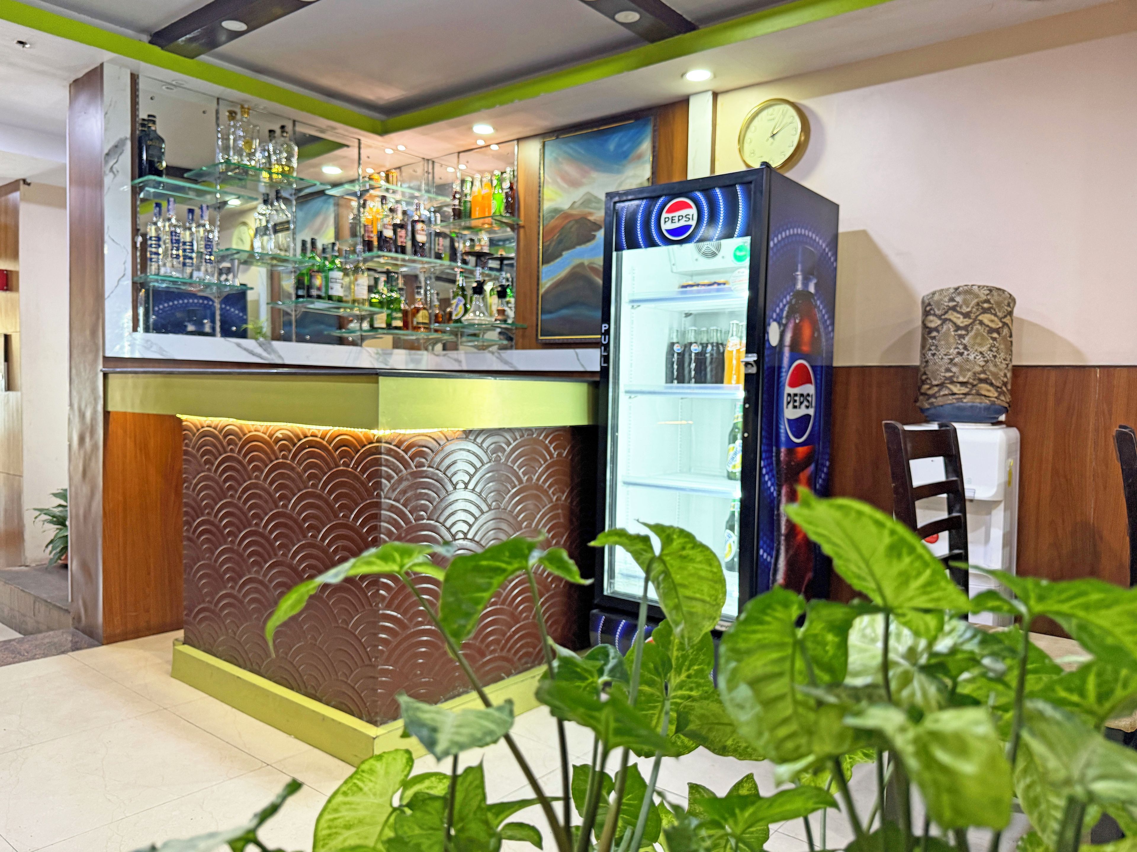 Una zona de bar con un refrigerador de Pepsi, estantes llenos de botellas y un revestimiento de pared estampado.