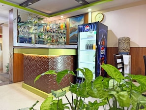 Una zona de bar con un refrigerador de Pepsi, estantes llenos de botellas y un revestimiento de pared estampado.