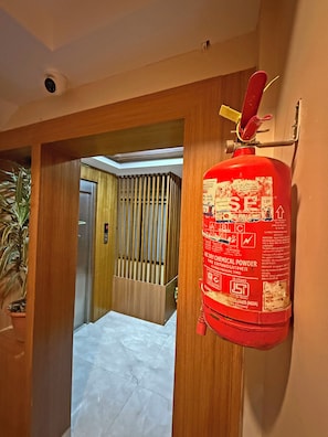 Extintor rojo montado en una pared en un pasillo con paneles de madera y una planta en maceta.