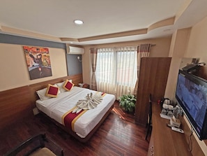 Una habitación de hotel con cama, televisión, planta y suelo de madera.