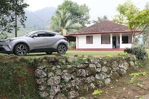 A stone wall, a house with a red roof, and a parked car.