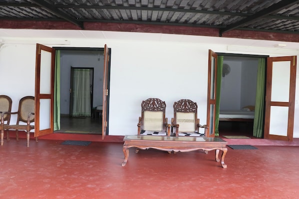 A room with a red floor, two wooden chairs, a small table, and an open door leading to another room.