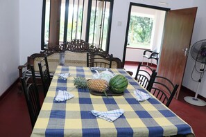 A dining area with a checkered tablecloth, a pineapple, a watermelon, and a fan. - Breathtaking Mountain & Rainforest Views / Cozy 2- Bed HilltopBungalow (SP)