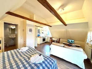 Ein Schlafzimmer mit einem Bett, einer Couch und einem Fernseher. Im Hintergrund ist eine Küche zu sehen.