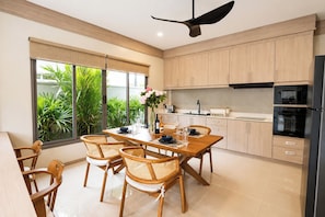 A modern kitchen with wooden cabinets, a dining table with chairs, and a ceiling fan. - Brand New 2BR Villa with Private Pool in Rawai (Tambon Rawai)