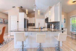 Cozinha moderna com ilha central, banquetas e iluminação pendente.
