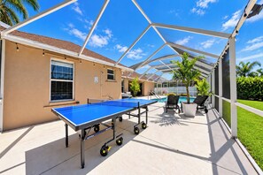 Área externa com piscina, mesa de pingue-pongue, cadeiras de descanso e um espaço de estar coberto.
