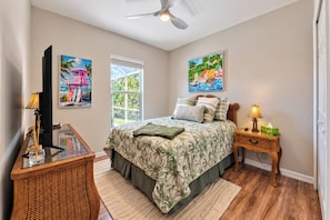 Quarto com cama, mesa de cabeceira, televisão e duas pinturas.