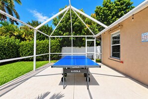 A ping pong table with a white frame and wheels, set up outdoors with a clear sky and greenery in the background. - VRCC Villa The Owl’s Nest (Cape Coral)