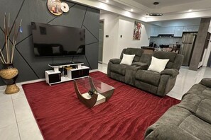 A modern living room with a flat-screen TV, a grey sofa, a red rug, and a glass coffee table. - 2-beds apartment in Westlands near GTC Free airport pick up with fitness access (Nairobi)