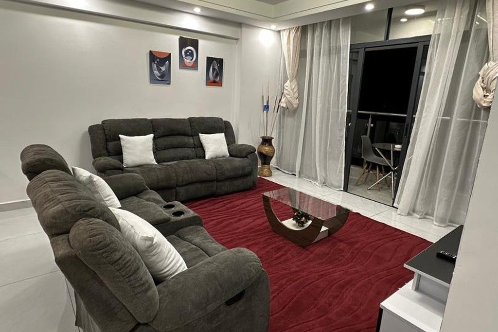 A modern living room with a sectional sofa, a glass coffee table, and a red carpet.