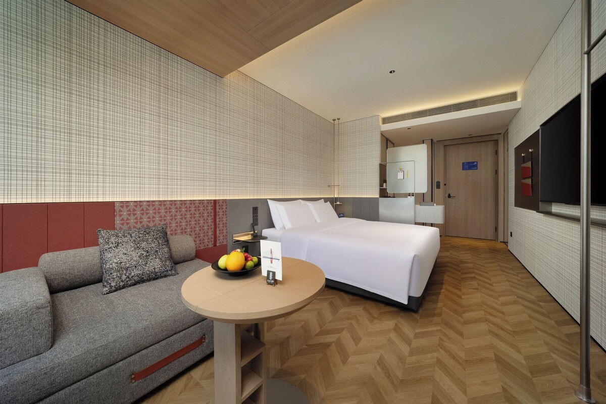 Een hotelkamer met een bed, een bank, een klein tafeltje met fruit en een televisie.