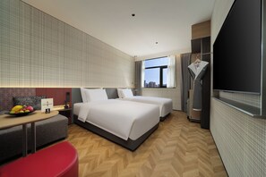 Een moderne hotelkamer met twee bedden, een bureau, een rode stoel, een schaal fruit en uitzicht op de stad.