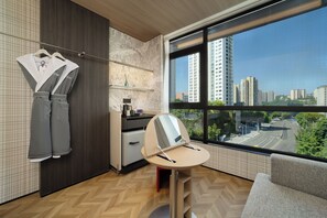 Een moderne hotelkamer met een groot raam, een bureau, een stoel en een garderobe met hangende kleding.