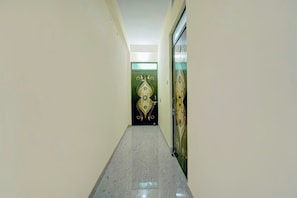 A corridor with a marble floor leading to a door with a decorative design. - Hotel O City View (Patna)