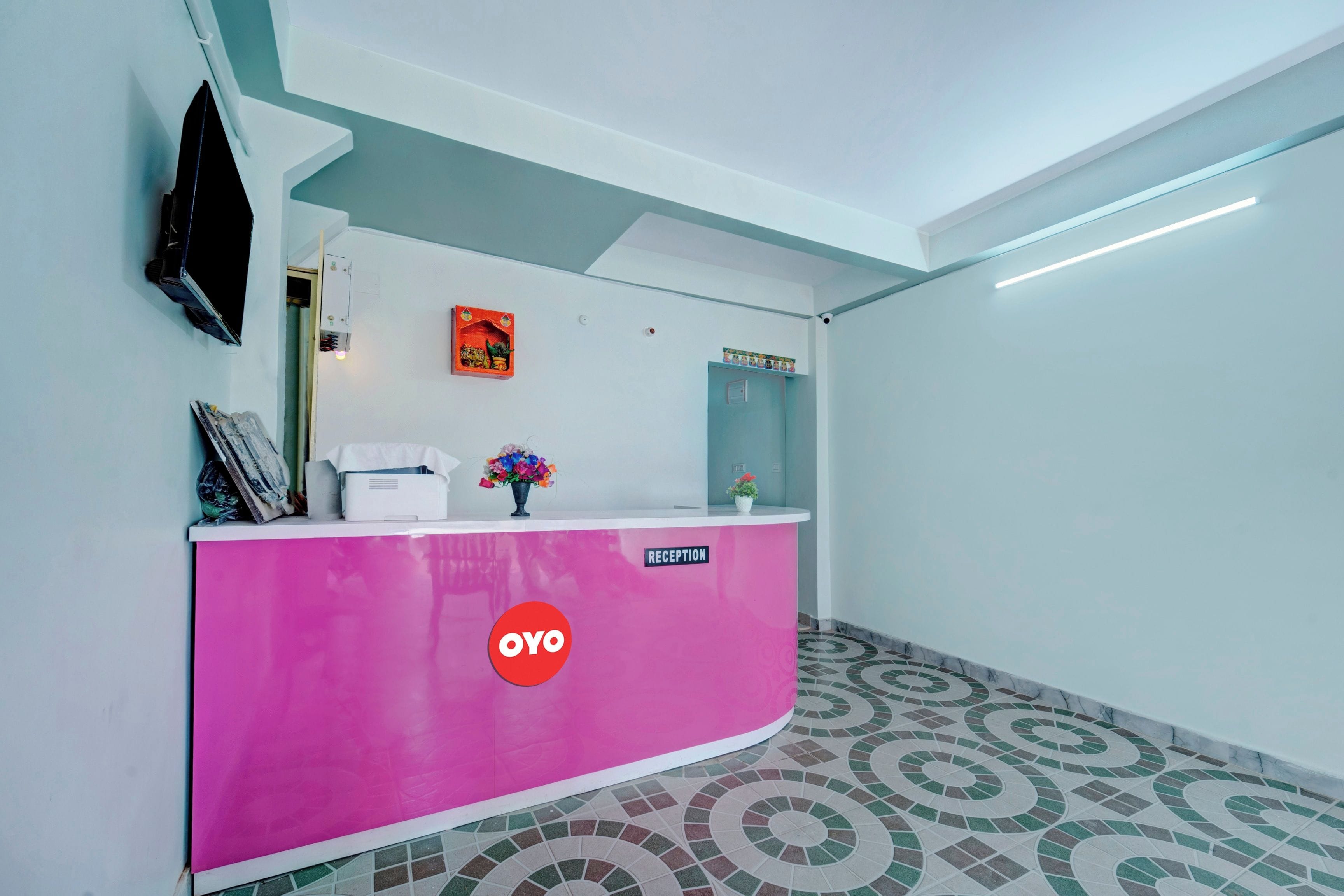 Una mesa de recepción con un letrero que dice 'Reception', el logotipo de 'OYO' y una planta en maceta.