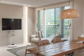 Ein modernes Wohnzimmer mit großem Fernseher, einem Esstisch und einem Balkon mit Blick.