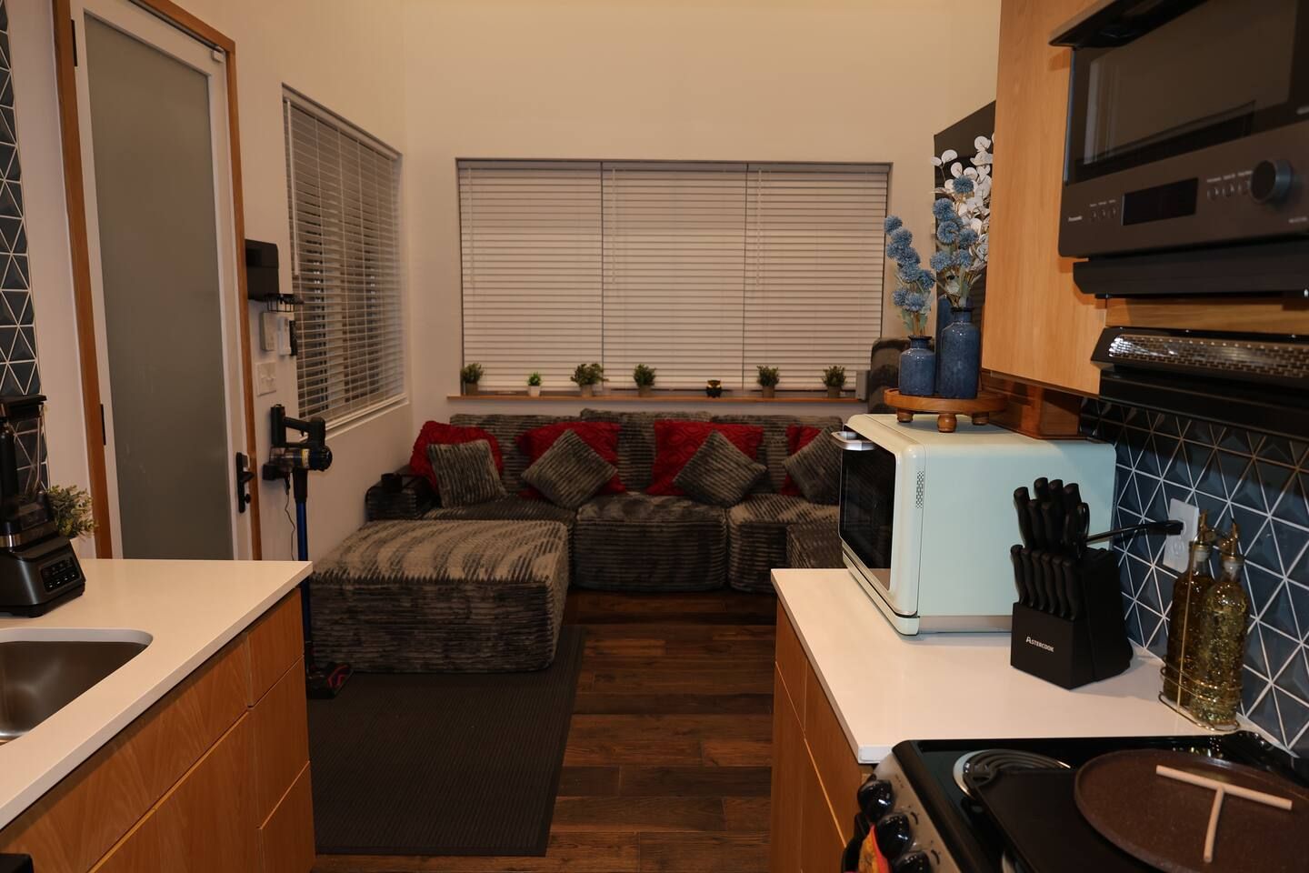 A compact kitchen with a built-in microwave, a stove, and a sink. There is a seating area with a sofa and cushions.