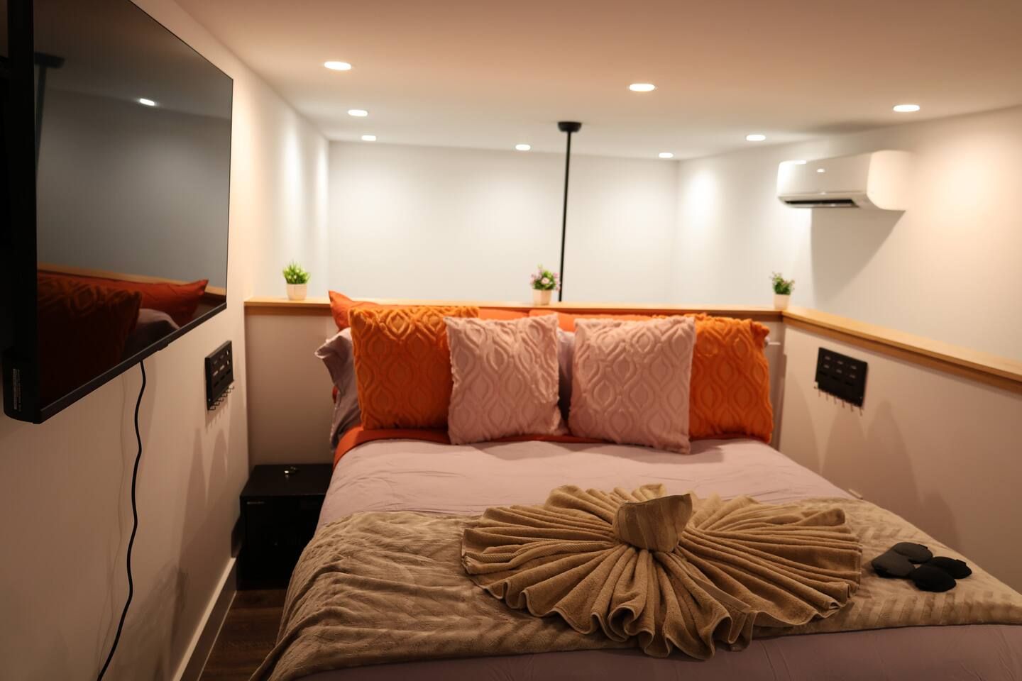 Ein Hotelzimmer mit Bett, Flachbildfernseher an der Wand, Nachttisch und Wandgerät zur Klimatisierung.