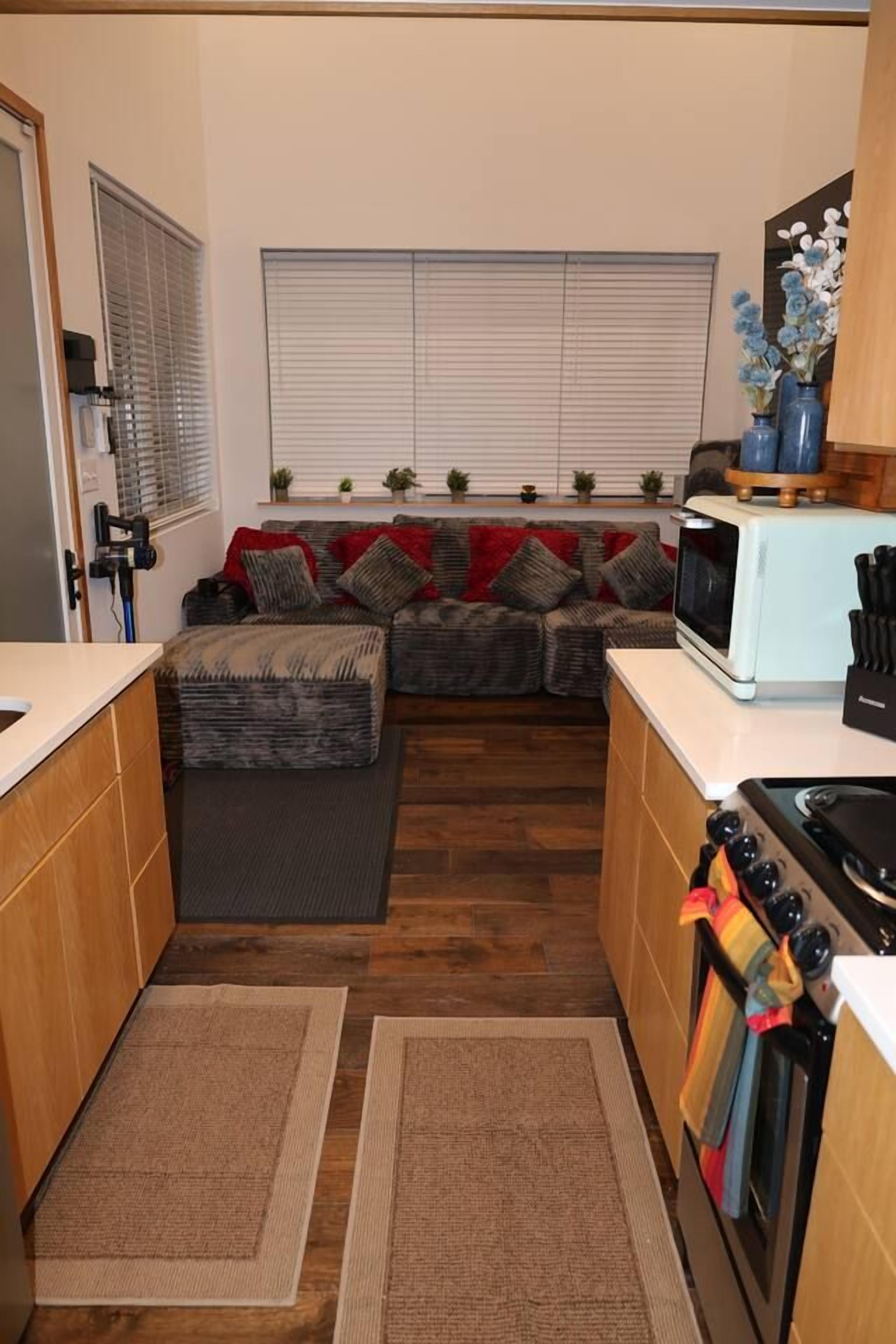 Eine kompakte Küche mit Mikrowelle, Herd und Backofen. Im Hintergrund befindet sich eine Couch mit Kissen.