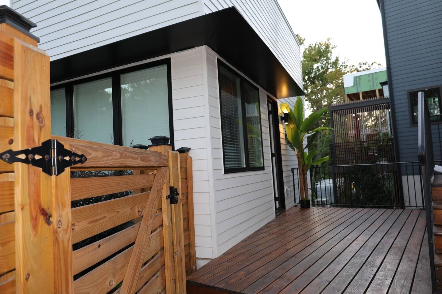 Una terraza de madera que conduce a una casa moderna con ventanas amplias y una reja de metal negro.