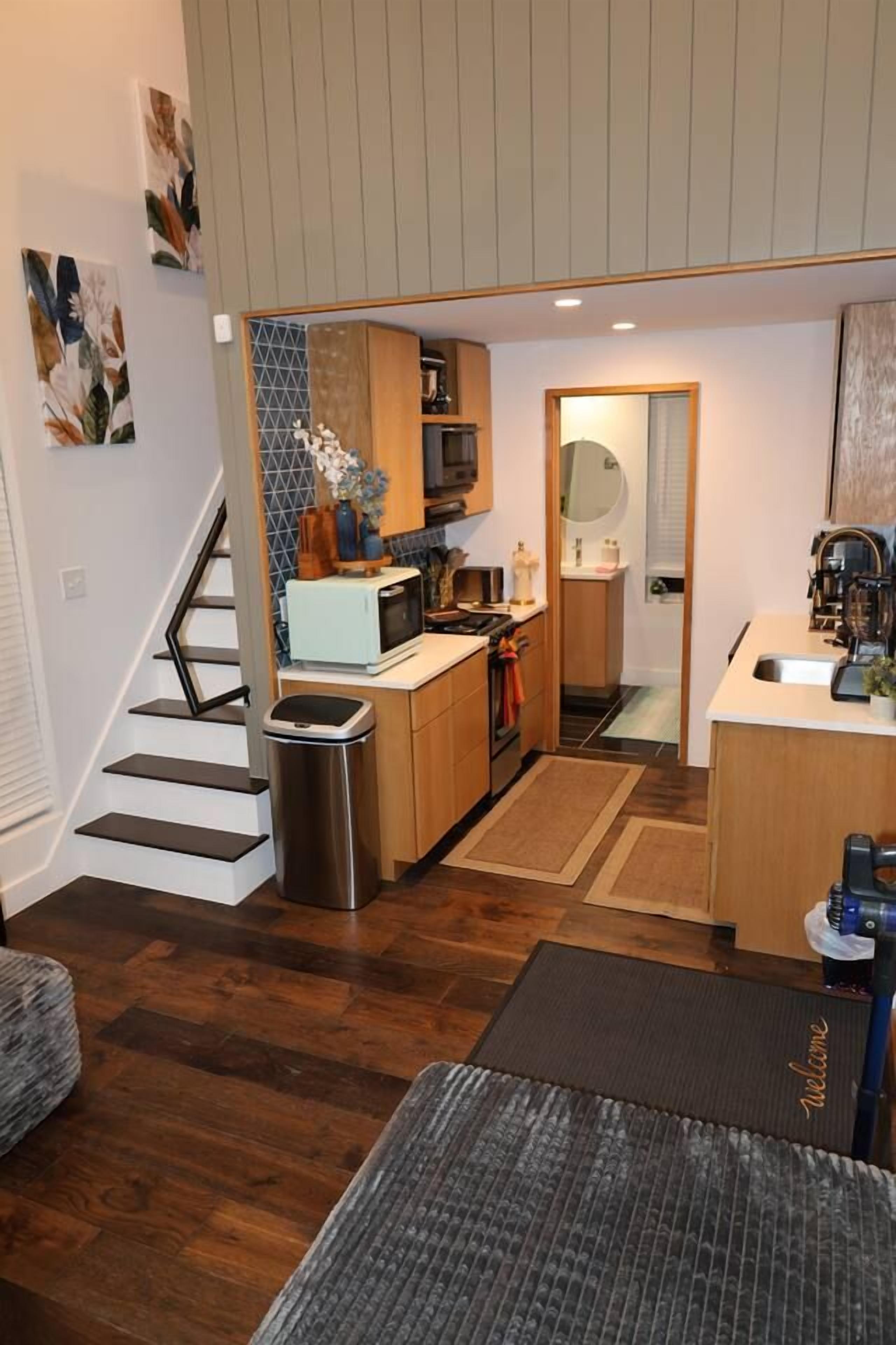 Cocina compacta con microondas, estufa y pileta, un pequeño basurero y una escalera que sube a un nivel superior.
