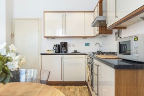A modern kitchen with white cabinetry, a coffee maker, a microwave, and a stove. - Home cinema and super king bed - Hampstead (Greater London)