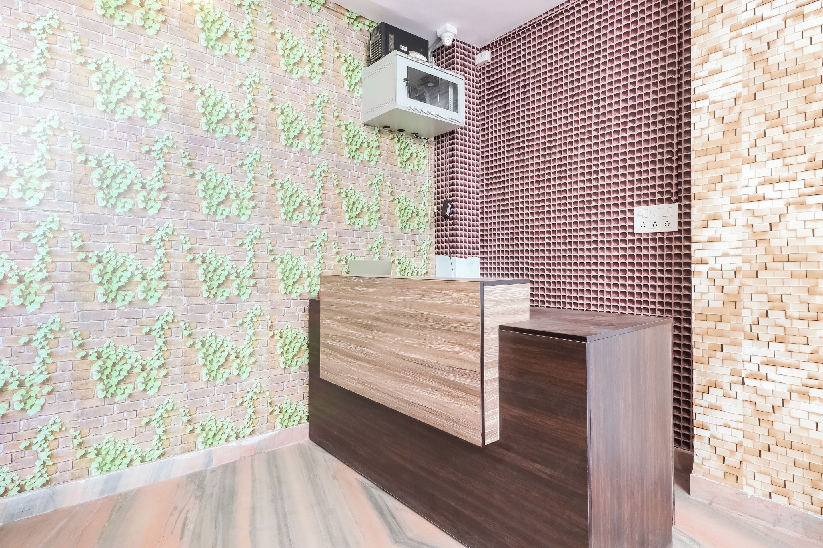 A reception area with a wooden reception desk, a brick wall with green foliage, and a patterned wall with a grid design.