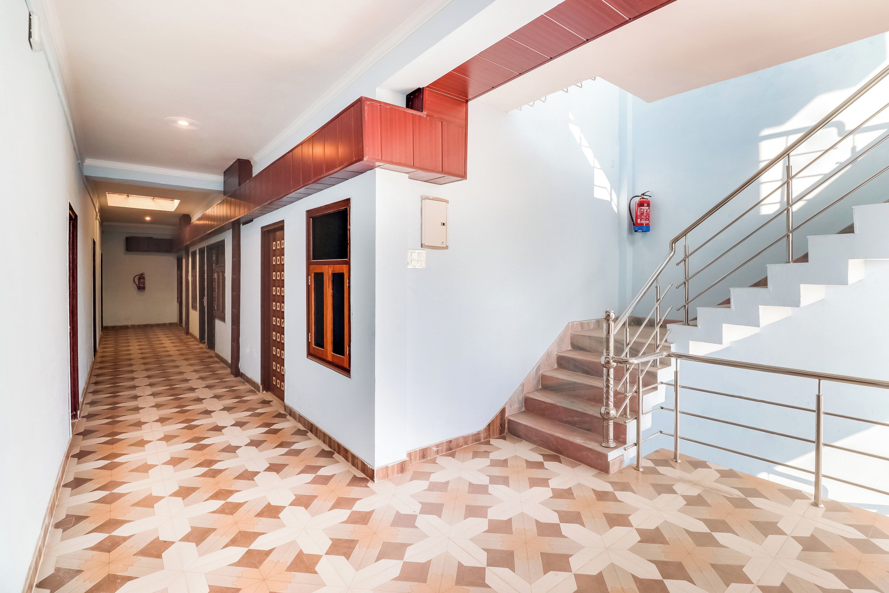 A hallway with patterned flooring, a staircase with metal railings, and a fire extinguisher mounted on the wall.