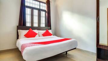 A neatly made bed with white linens and red accents, a window with curtains, and a wooden floor.
