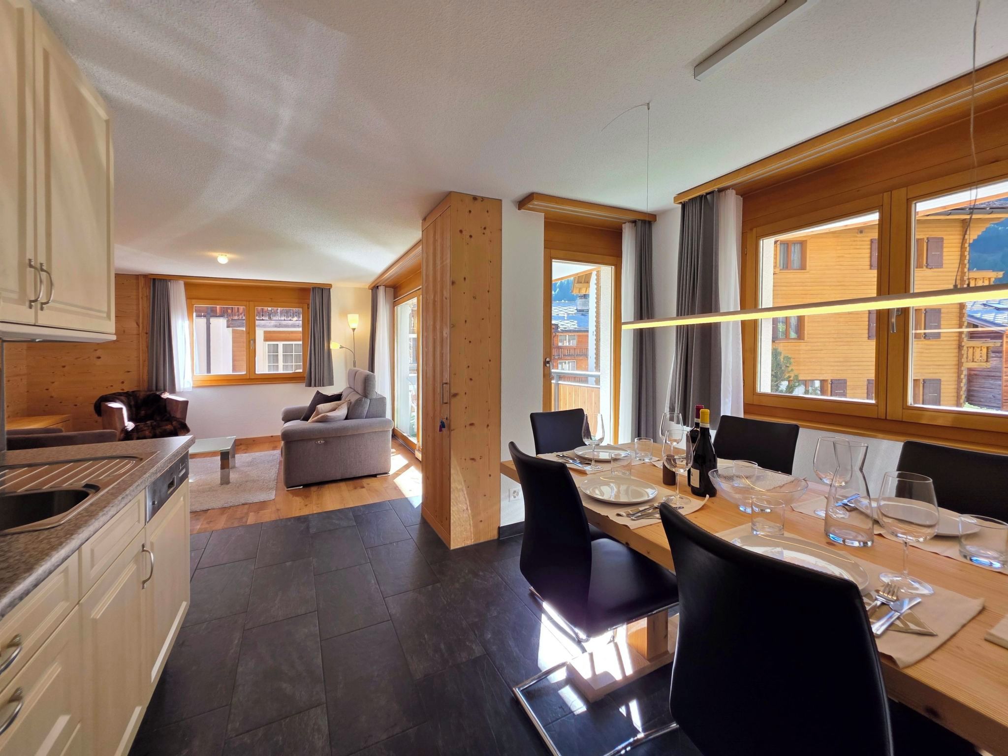 A modern kitchen with a dining area, wooden walls, and large windows.