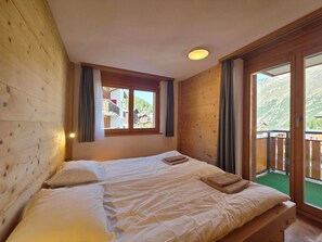 Una habitación con paredes de madera, una cama con ropa de cama blanca, una ventana con cortinas y vistas a un paisaje montañoso.