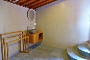 A bathroom with a wooden vanity, a sink, a mirror, and a stone-tiled floor.