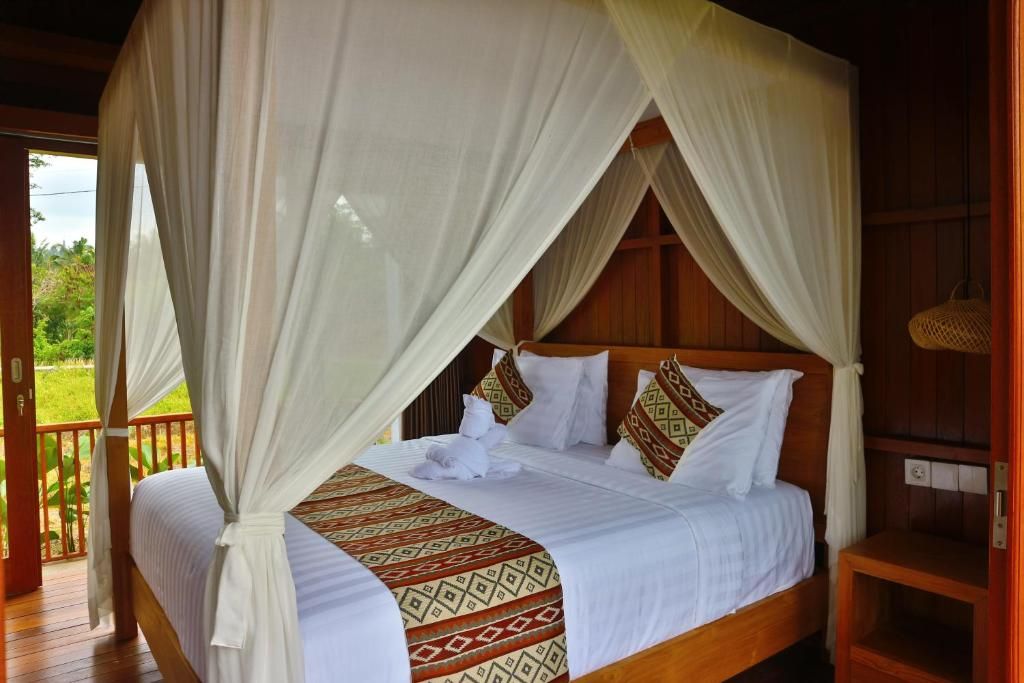 Una cama con dosel y cuatro columnas, con un edredón estampado, un cabecero de madera y vistas al exterior.