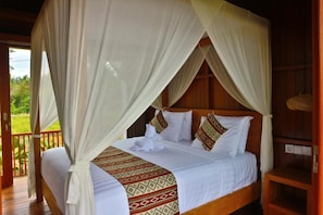 A four-poster canopy bed with a patterned bedspread, a wooden headboard, and a view of the outdoors.