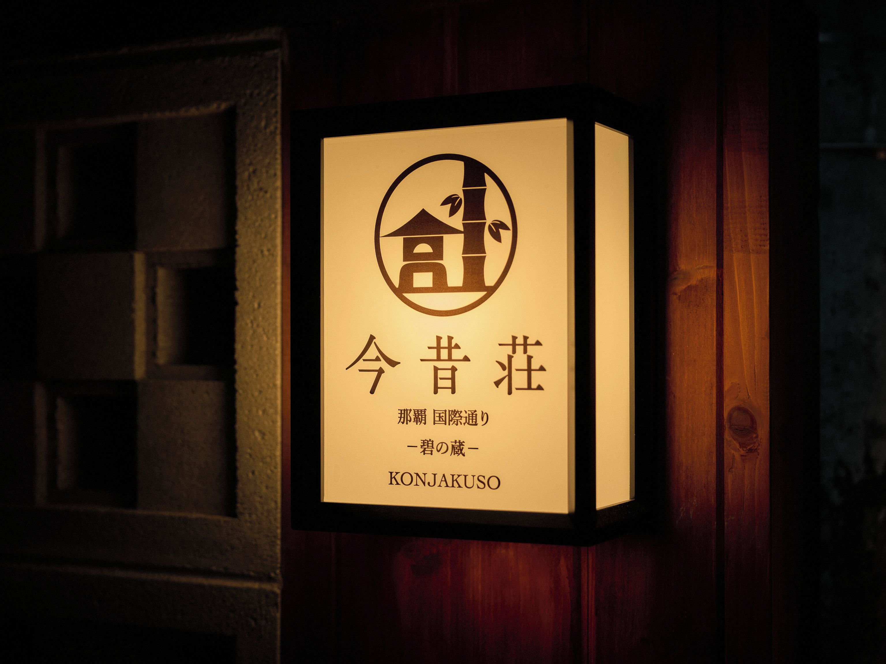 Un letrero en marco con caracteres japoneses y un logotipo, fijado en una pared de madera.