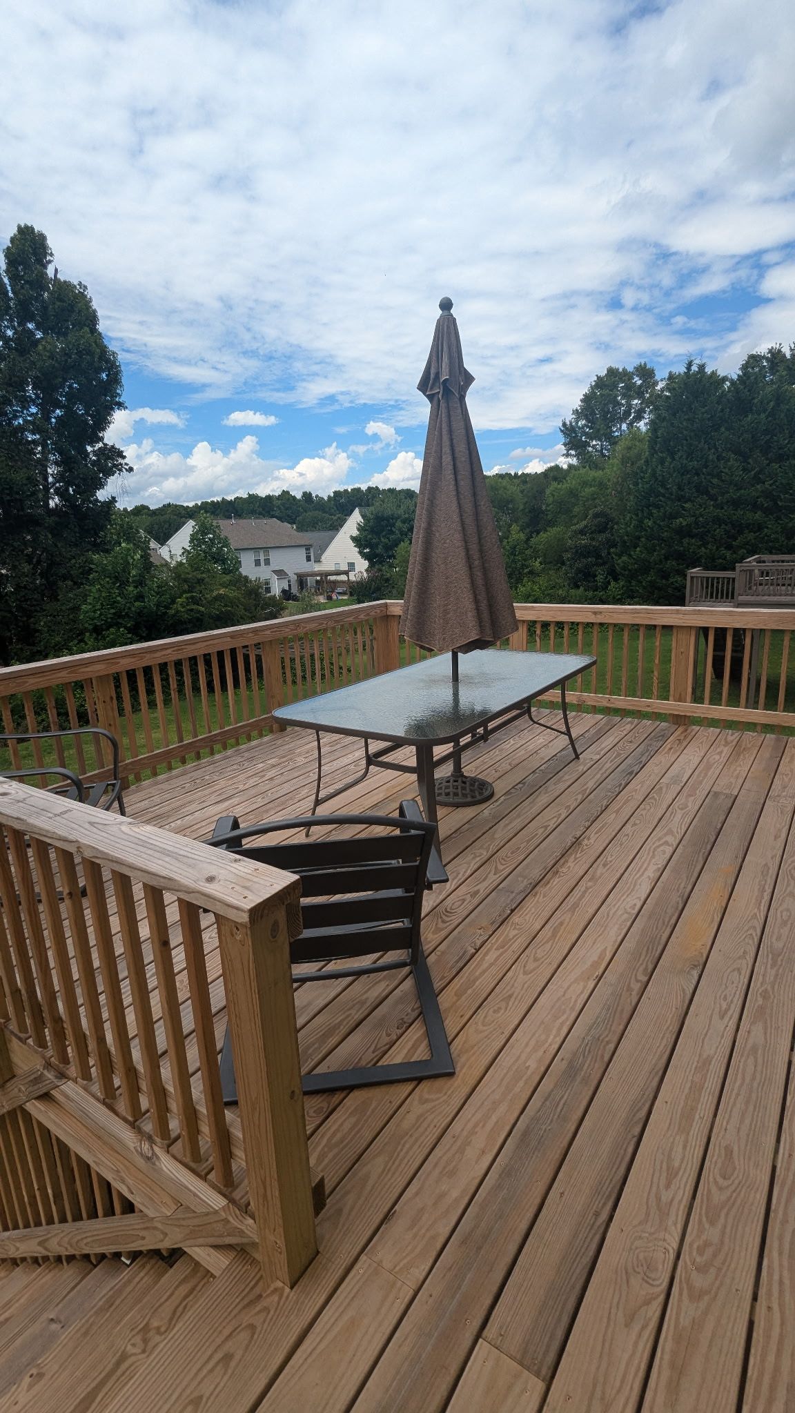 A wooden deck with a glass table and metal chairs, surrounded by a wooden railing.