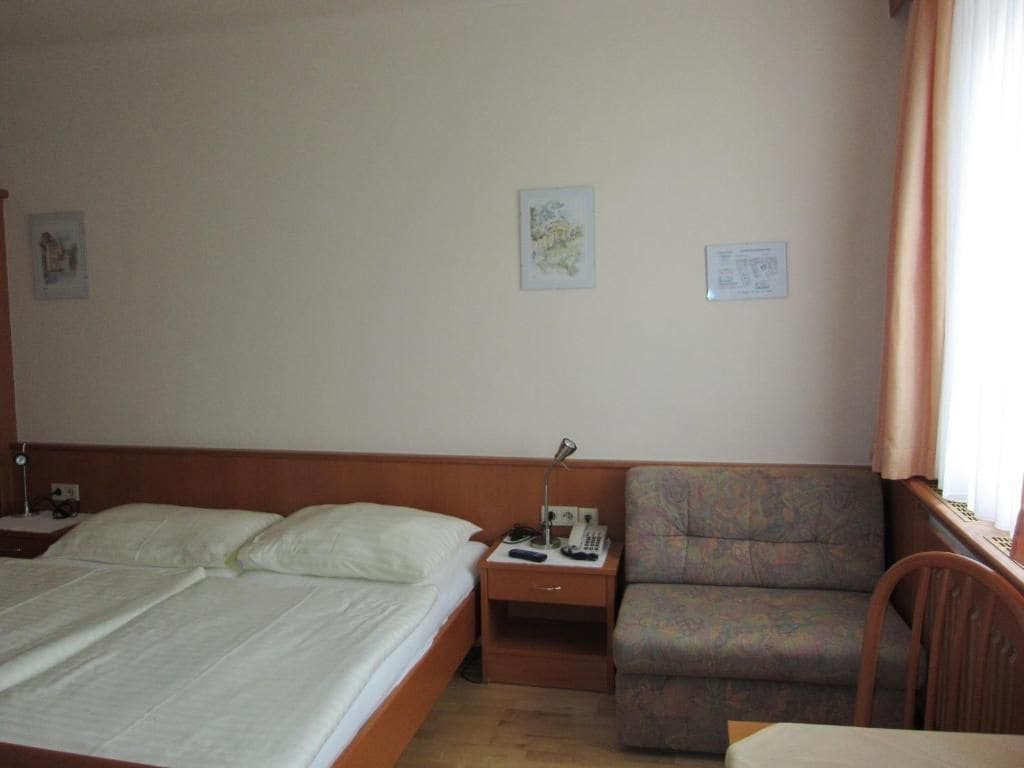 A hotel room with a bed, a nightstand, a telephone, a chair, and a small table.