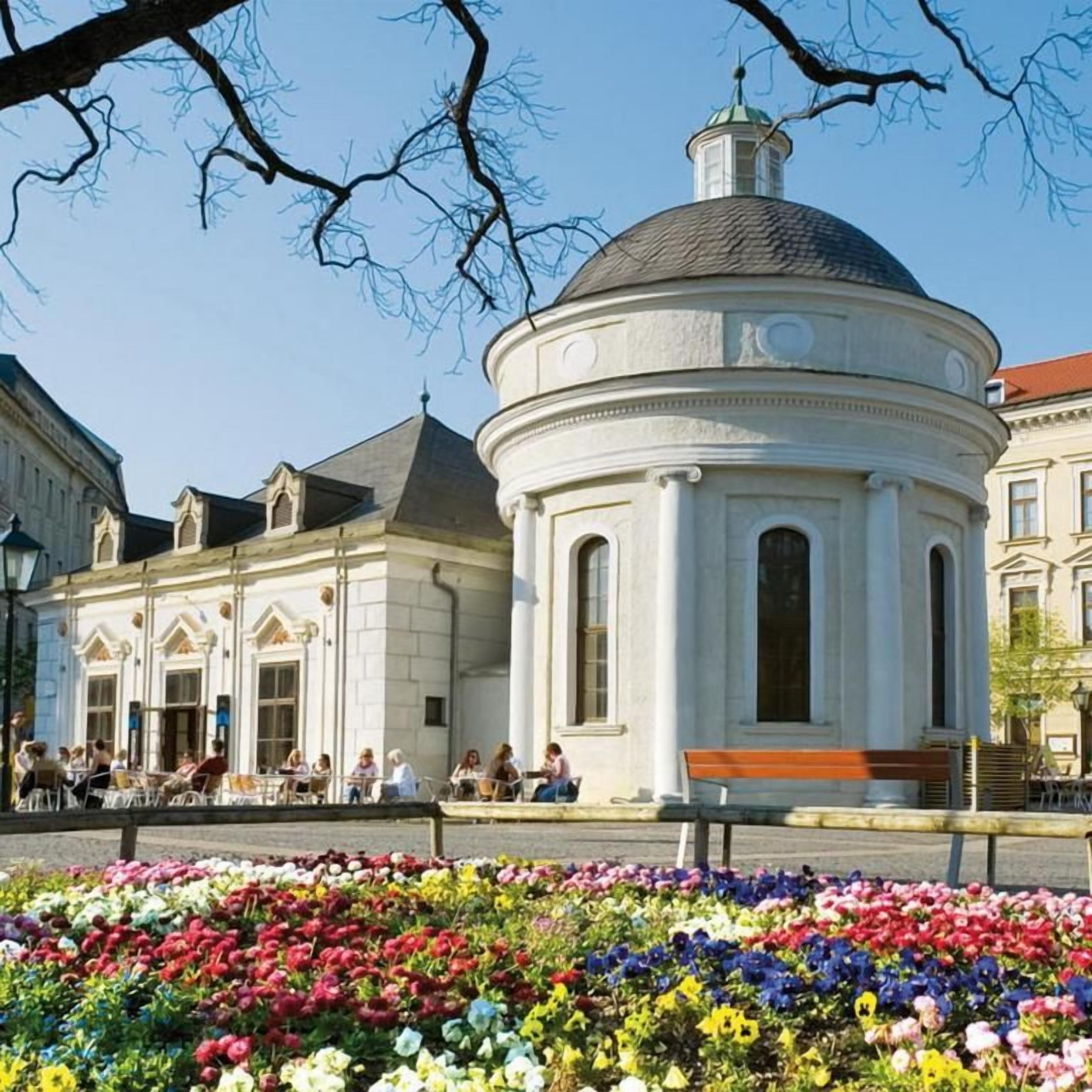 Un edificio histórico con una cúpula y arquitectura clásica, rodeado de un jardín lleno de flores.