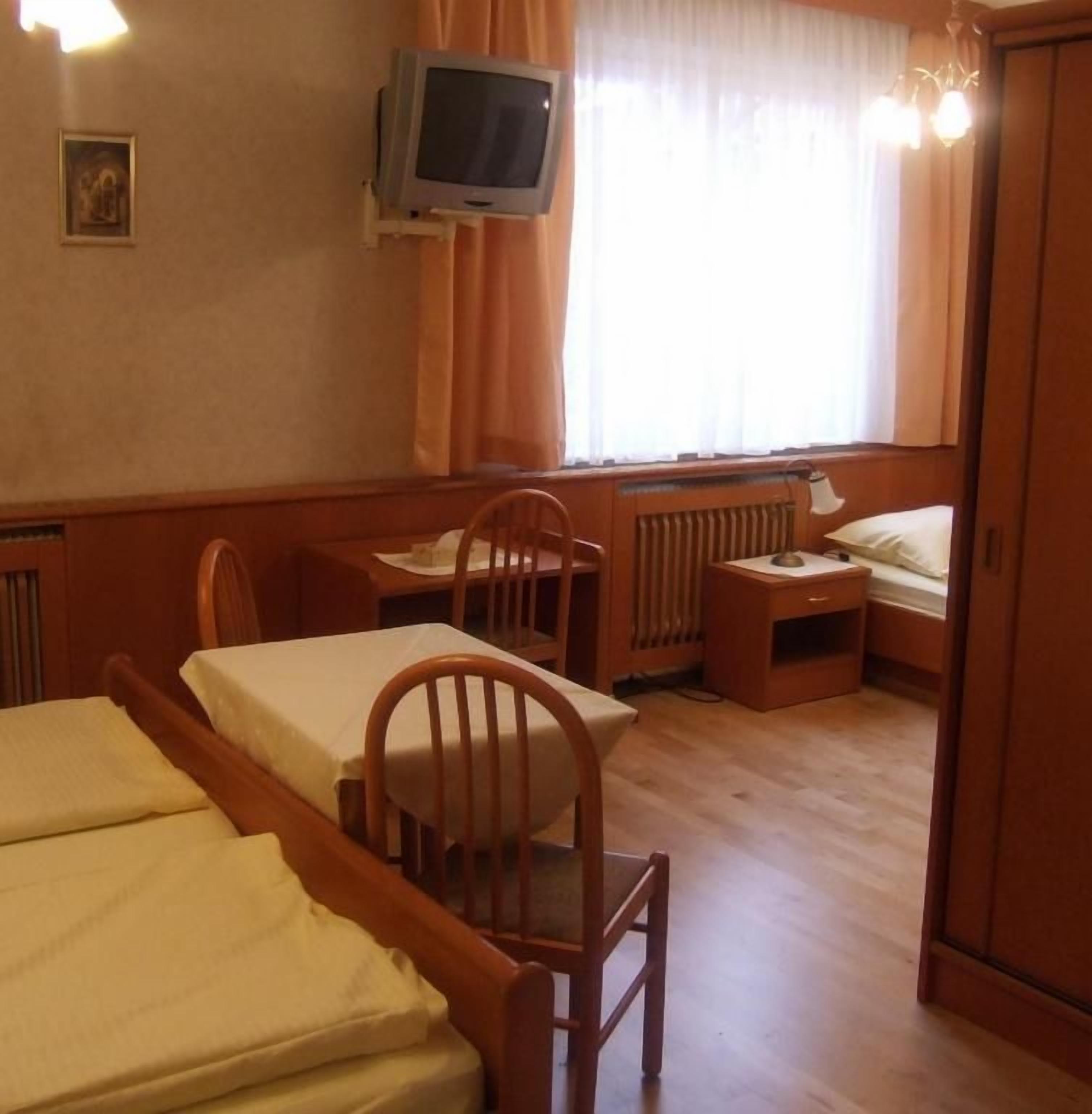 Une chambre avec deux lits, un bureau, une chaise, une télévision et une fenêtre avec des rideaux.