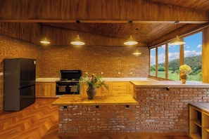 A kitchen with a brick wall, wooden ceiling, and a large window with a view of the outdoors.