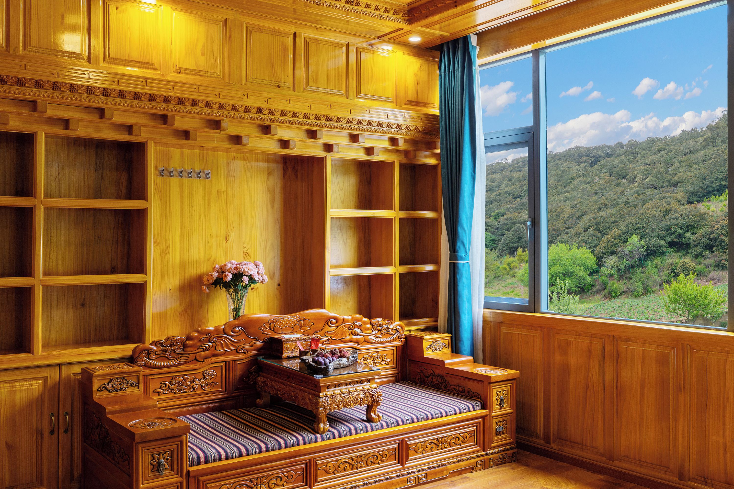 A traditional wooden room with a built-in sofa, a window with a view of a forest, and a decorative vase with flowers.