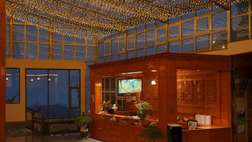 Een receptiegedeelte met een houten balie, een televisiescherm en een groot raam met uitzicht op de stad.