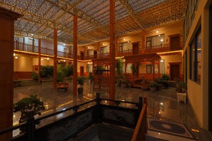 Un amplio atrio interior con techo alto decorado con guirnaldas de luces, múltiples balcones y una variedad de plantas en macetas.