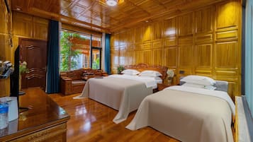 A hotel room with two beds, wooden flooring, a wooden ceiling with a skylight, and a view of greenery outside.