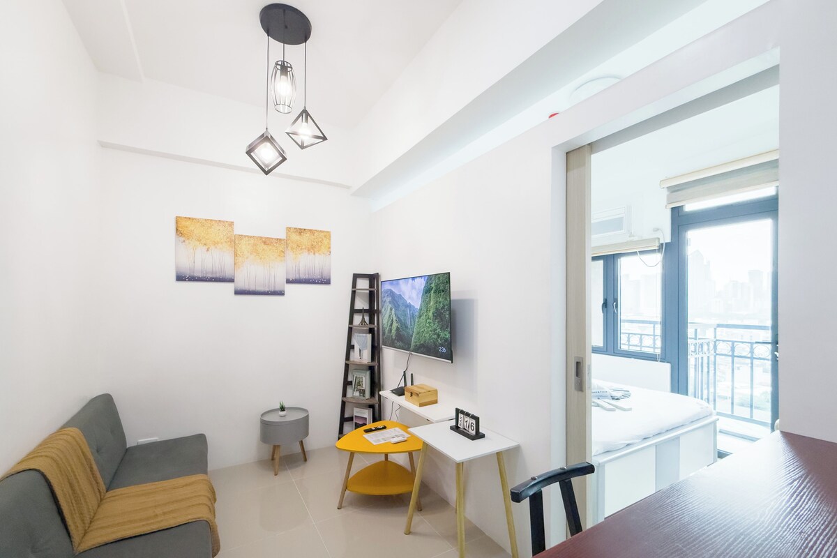 Una sala de estar moderna con un sofá gris, una mesa de comedor de madera, un televisor y obras de arte en las paredes.