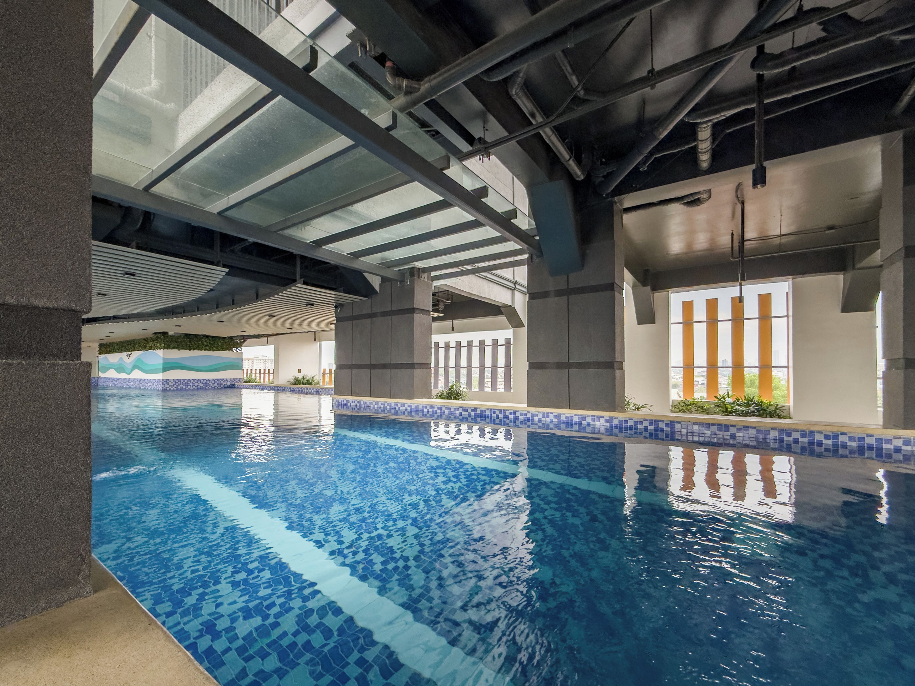 An indoor swimming pool with clear blue water, surrounded by a tiled edge and a concrete floor.